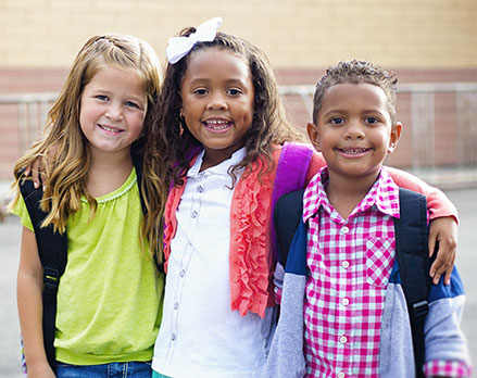 Three elementary school children leaning towards each other and smiling at the camera.